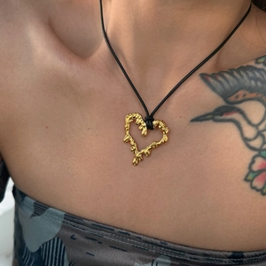 Detail of molten gold heart pendant with black cord chain worn on model with tattoos