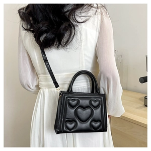 Détail d'un sac à bandoulière noir avec motif cœurs gaufré et finitions dorées