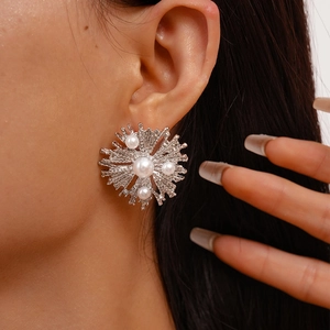 Detail of silver metallic flower earrings with pearls worn by a model in a close-up view