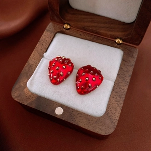 Macro detail of red strawberry earrings with gold accents in a premium wooden jewelry box