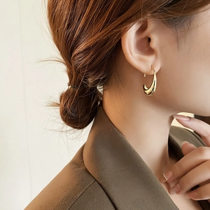 Close-up of elegant 14k gold plated oval metal drop earring on model ear profile