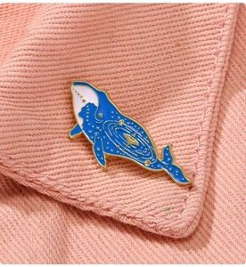 Macro detail of blue whale enamel brooch with starry sky pattern on pink knit fabric