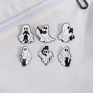 Close-up of Halloween ghost and black cat enamel pins displayed on white canvas fabric