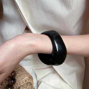 Detail of a minimalist wide black glossy resin bangle worn on a wrist for a resort style look