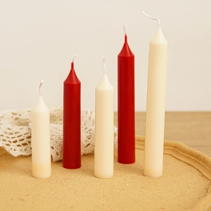 Tall slender red and white tapered candles in various heights on a wooden base