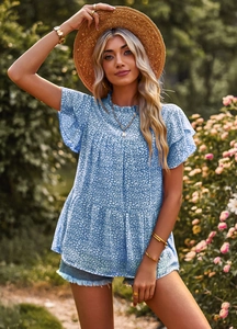 Detail of floral printed top featuring flutter sleeves and a layered hem in a garden setting