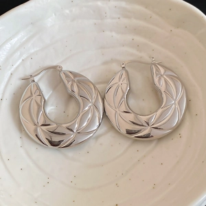 Macro detail of silver textured hoop earrings with geometric star patterns on ceramic