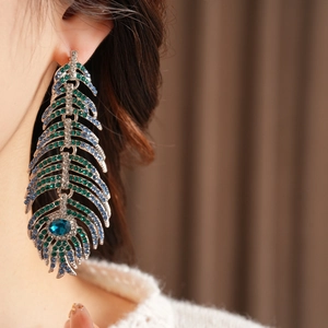 Detailed macro view of vintage feather drop earrings with emerald and sapphire rhinestones