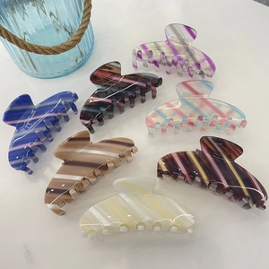 Flat lay of colorful striped acetate claw clips in various candy colors on white surface