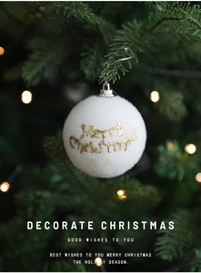 Close-up of white flocked Christmas ball with golden Merry Christmas text on tree branch