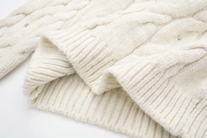 Detail des Zopfmusters am weißen Pullover mit dezenten Strasssteinen und Rippbündchen