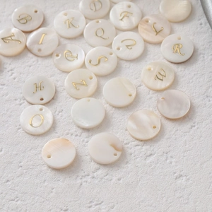 Macro shot of circular shell alphabet pendants with gold gothic letters for DIY jewelry