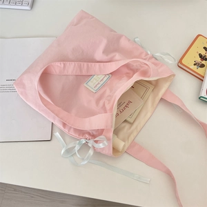 Detail of pink canvas tote featuring a white satin bow and interior logo label on desk