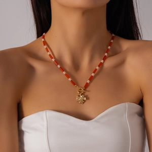 Detail shot of a beaded necklace with red and white beads and a golden maple leaf pendant