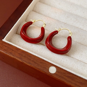 Macro view of gold-plated U-shaped hoop earrings with red enamel in a velvet jewelry box