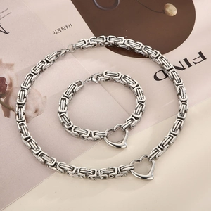 Silver Byzantine chain necklace and bracelet set with heart charms on a beige background