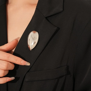 Nahaufnahme einer silbernen Tropfenbrosche am Revers eines schwarzen Anzugjackets