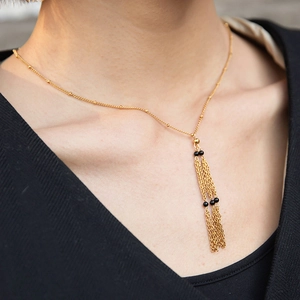 Close-up of golden stainless steel Y-chain necklace with black bead tassel on model