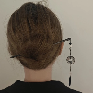 Detail of elegant black hair pin with pearl tassel worn in a low bun hairstyle