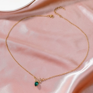 Detail of gold crown necklace with green teardrop gemstone on pink silk background
