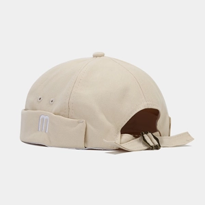 Detail of beige canvas docker hat featuring M embroidery and bronze adjustable buckle