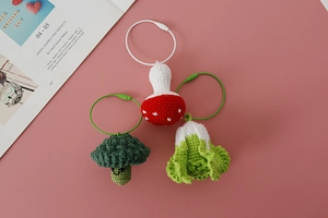 Handmade crochet keychains featuring smiling broccoli, red mushroom, and cabbage on pink base