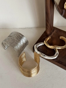 Detail of wide irregular golden and silver textured open arm cuffs on wooden stand