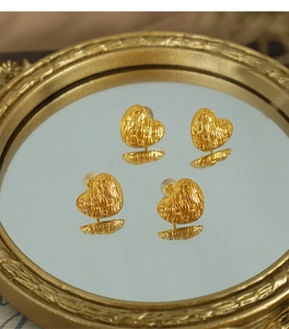 Detailed macro view of four golden woven heart earrings on a vintage mirror tray