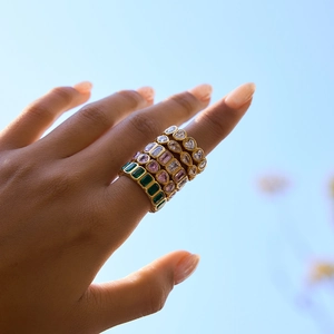 Stacked gold rings set with green emerald-cut and pink heart zircons on finger