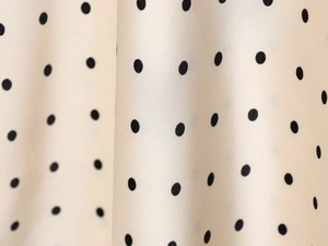 Détail du tissu satiné brillant à pois noirs sur fond crème montrant une texture lisse