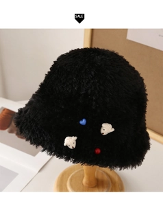 Detail of plush black faux fur bucket hat with cute bear and heart patches on wooden stand