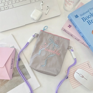 Détail du sac bandoulière en toile grise brodée avec bandoulière tressée lilas sur bureau