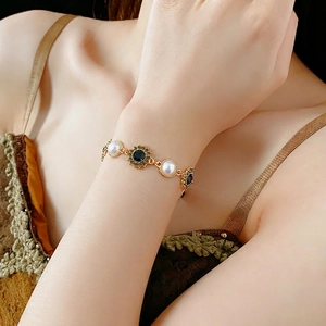 Vintage style gold bracelet with artificial pearls and black stones on a female wrist
