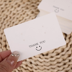 Handheld view of white THANK YOU earring display card with smiley face print