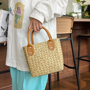 Detail of straw woven tote bag with brown leather handles held by model in casual setting