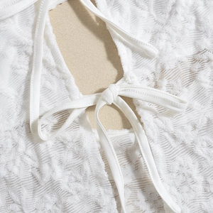Detail of white lace top featuring floral jacquard texture and delicate bow tie closure