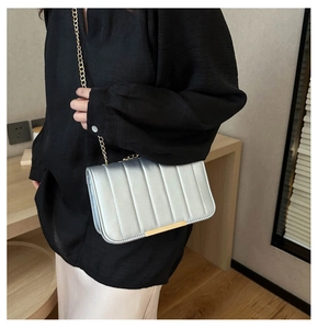 Silver shoulder bag featuring vertical quilting, gold chain strap, and metallic bar detail