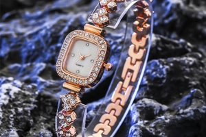 Vue détaillée d'une montre carrée en or rose avec strass pour femme sur roche sombre