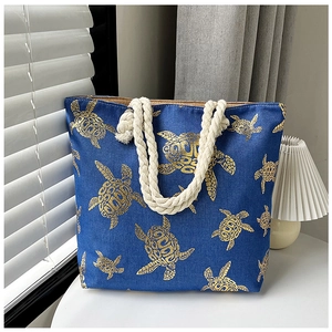 Detail of blue tote bag with gold turtle print and beige rope knot handle on white desk