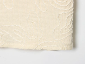 Détail du tissu en coton et lin blanc cassé avec broderie ondulée blanche délicate
