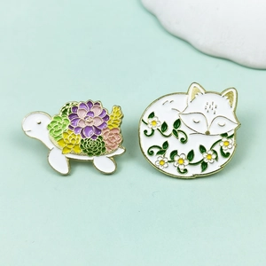 Close-up of enamel turtle and sleeping fox pins with floral patterns on mint green background