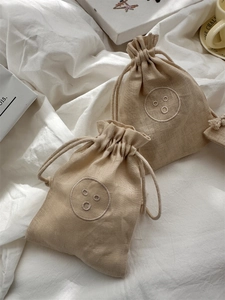 Linen drawstring bags with embroidered smile designs in a natural cream and beige finish