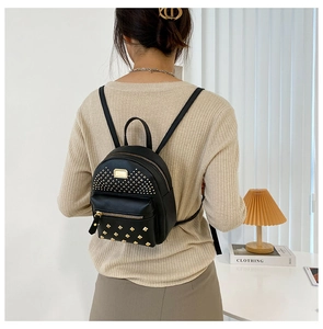 Detail of a black faux leather mini backpack featuring golden rivets and metal plate