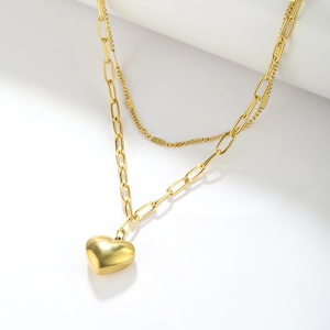 Detail of layered gold paperclip chain necklace with a 3D heart pendant on white surface