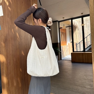 Model wearing a large cream pleated tote bag featuring a small Sunshine label