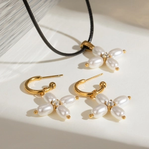 Close-up of pearl flower earrings and cross pendant necklace on a stone background
