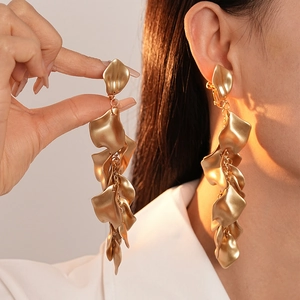 Detail of matte gold pleated petal tassel clip-on earrings on a model with sunset lighting