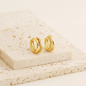 Close-up of gold double-hoop earrings with pave-set crystals on a stone prop
