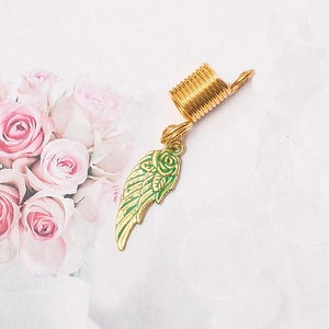 Detail view of golden spring dreadlock ring with green enamel wing charm and metal texture