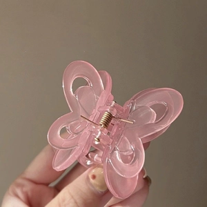 Close-up of a pink acrylic butterfly hair claw clip held against a soft background